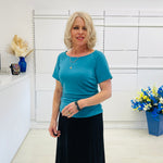 Woman in a blue top and black skirt standing in a room with white walls and decorative elements.