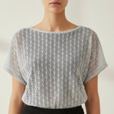 Woman wearing a gray lace top against a plain background