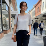 Woman walking on a city street wearing a light gray sweater and black pants.