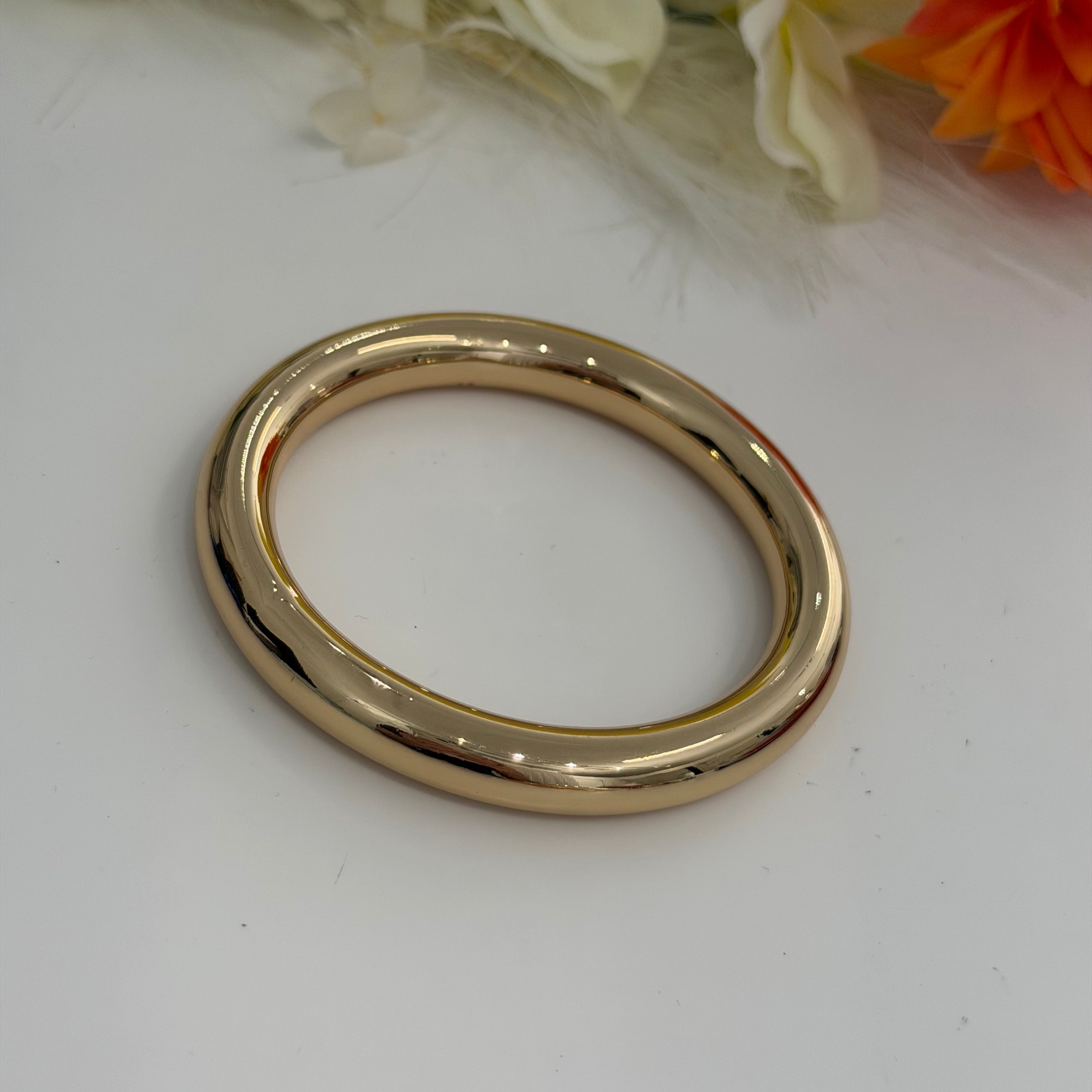 Gold bracelet on a white surface with flowers in the background