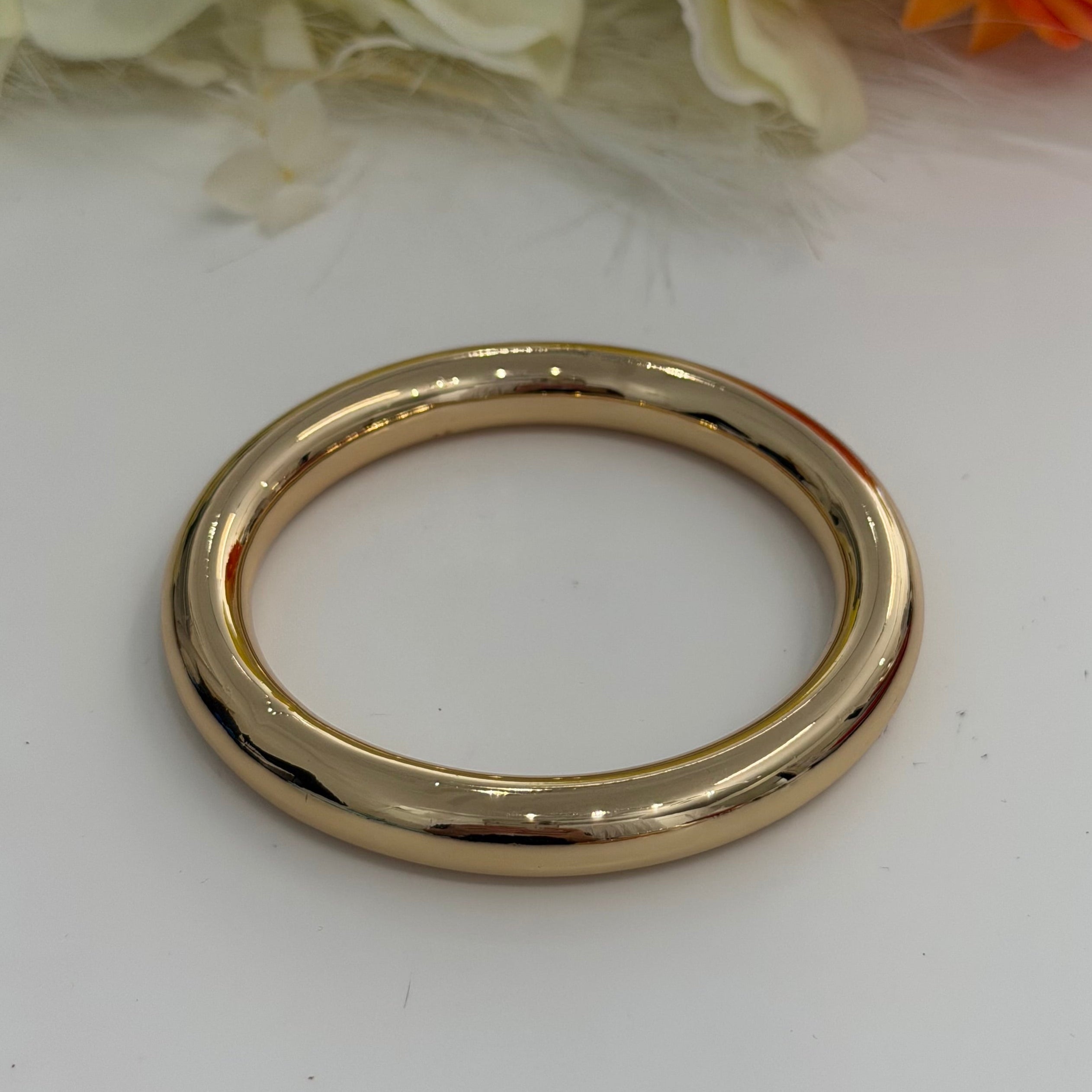 Gold bracelet  on a white surface with flowers in the background