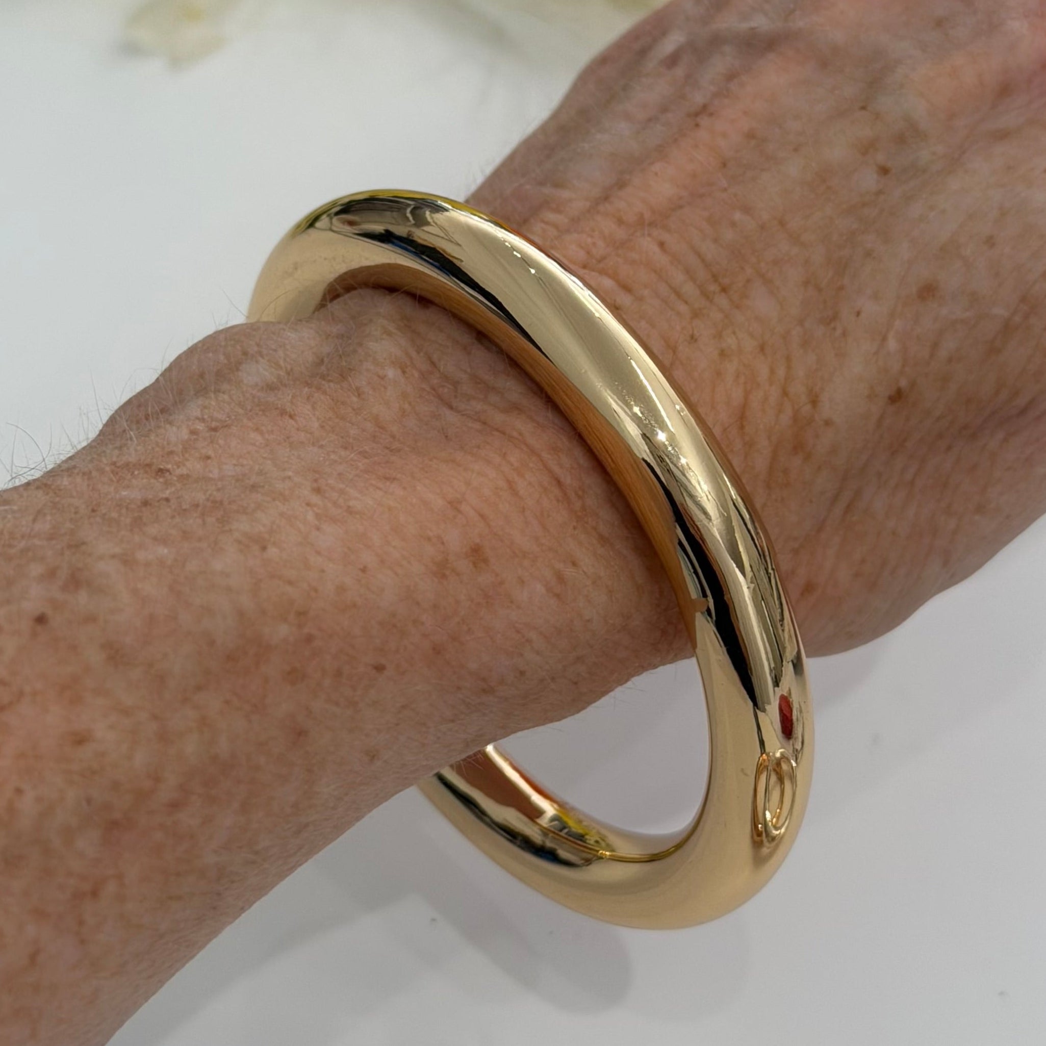 Gold bracelet on a wrist with flowers in the background
