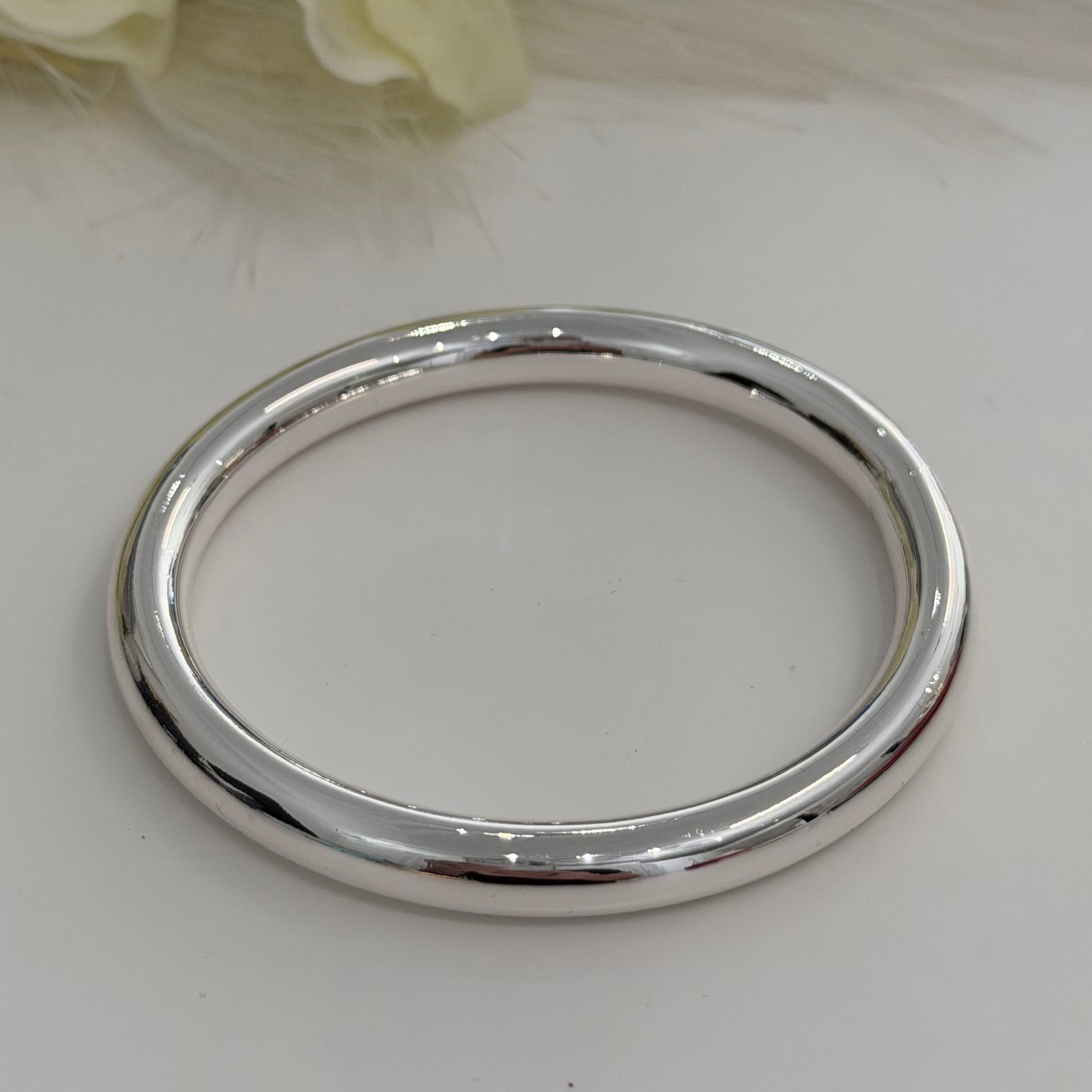 Silver bracelet on a white surface with flowers in the background