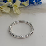 Silver bracelet on a white surface with blurred flowers in the background