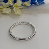 Silver bracelet on a white surface with blurred flowers in the background