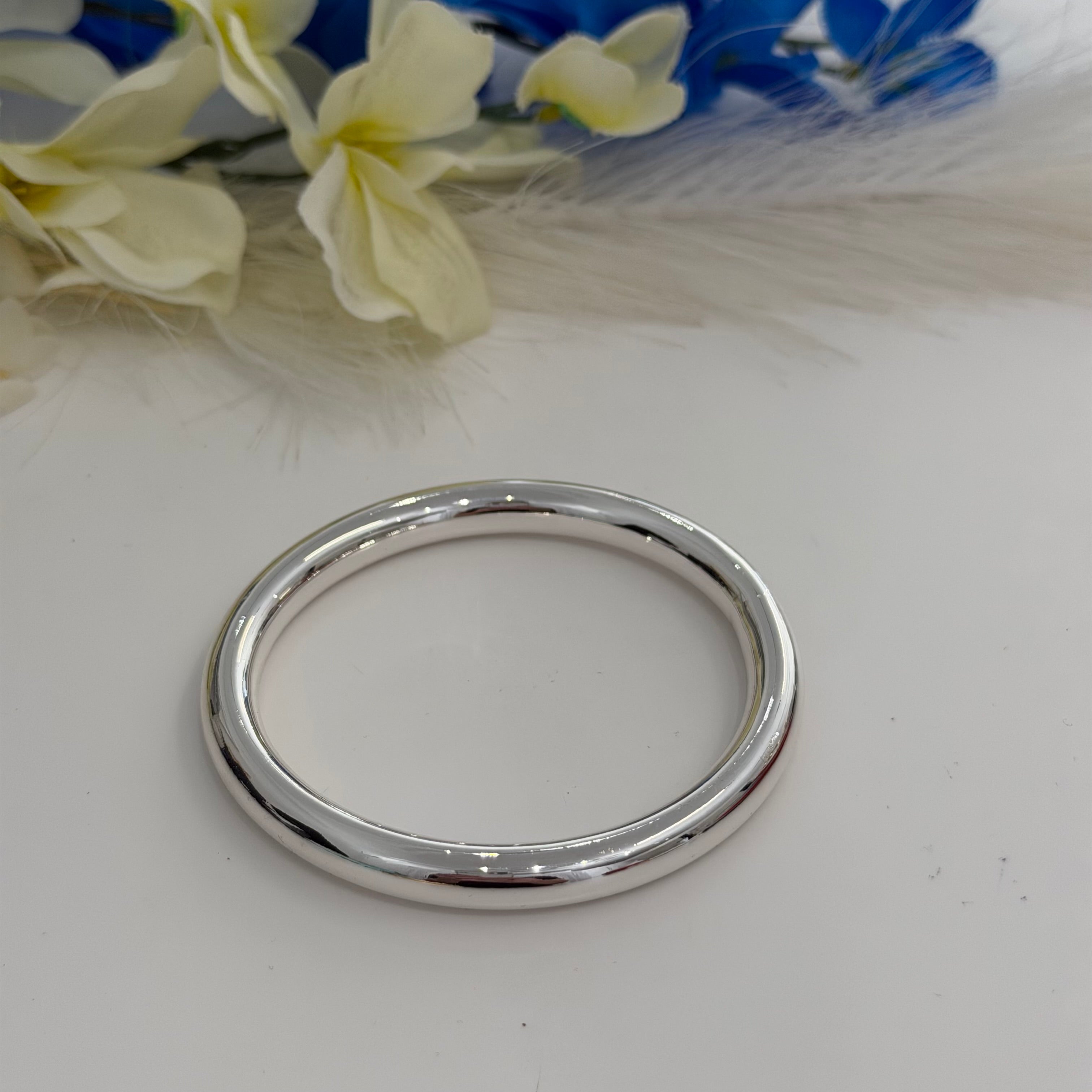 Silver bracelet on a white surface with blurred flowers in the background