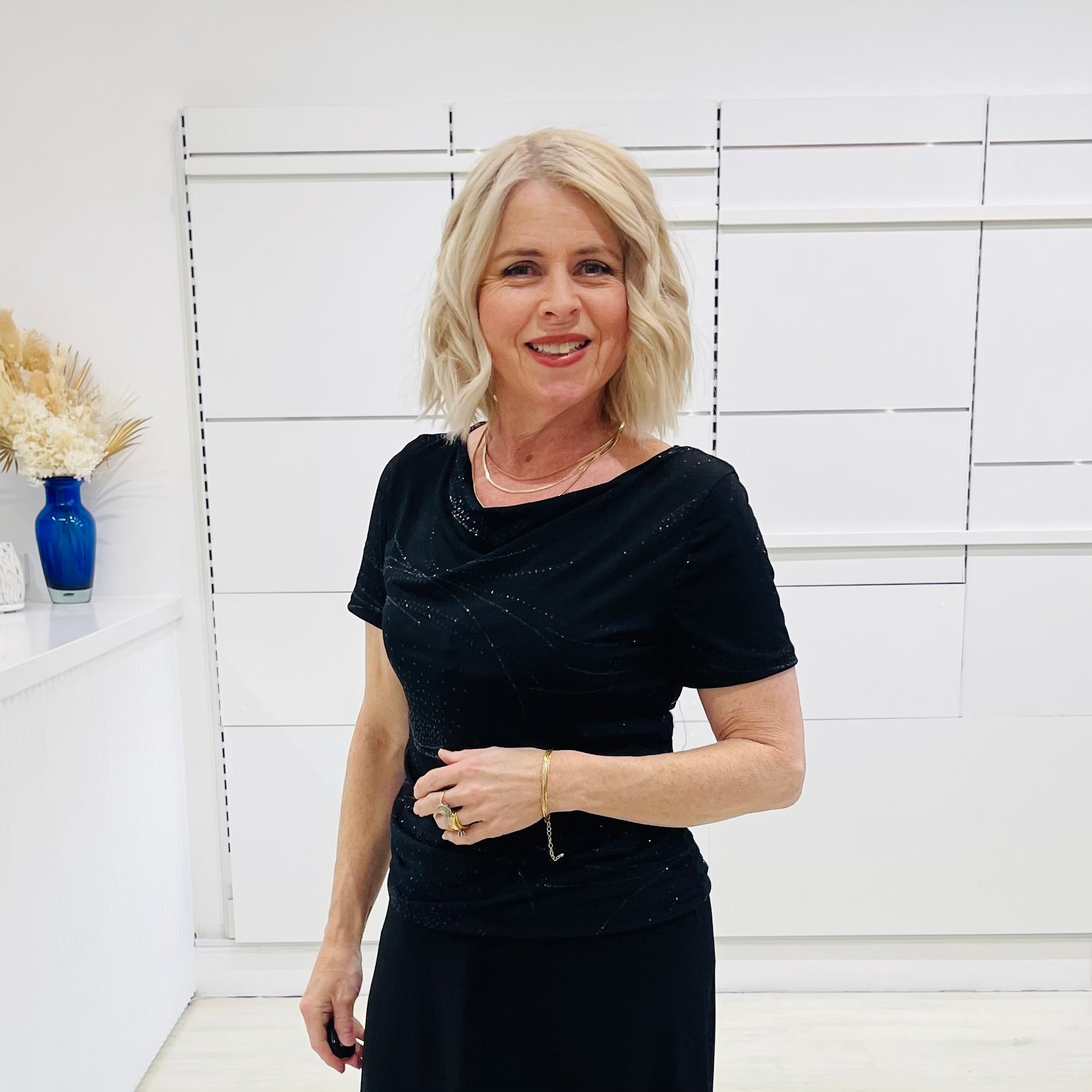 Woman in a black dress standing against a white wall with decorative elements.