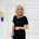 Woman in a black dress standing against a white wall with decorative elements.