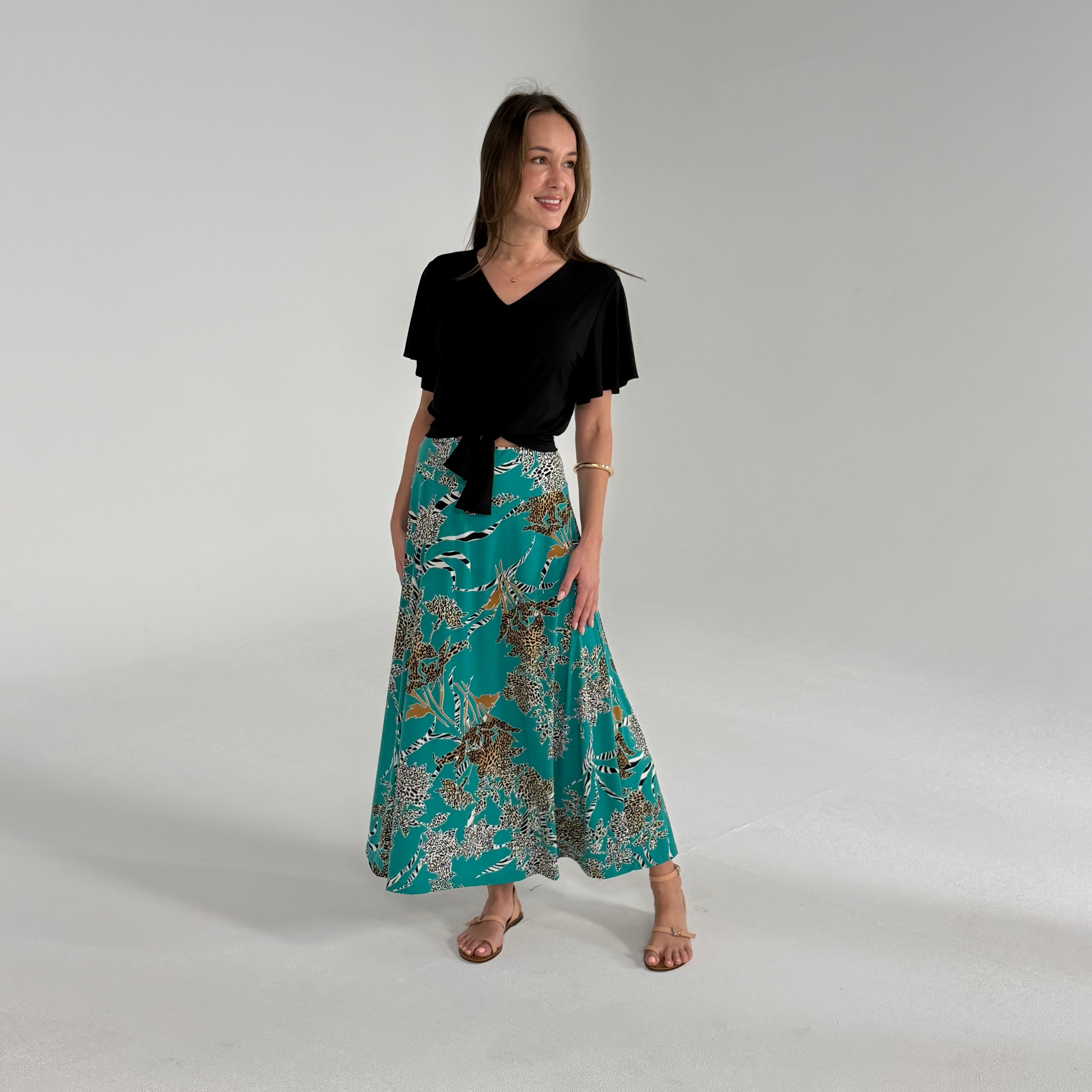 Woman wearing a black top and teal patterned skirt on a gray background