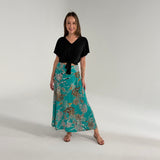 Woman wearing a black top and teal floral skirt on a plain background
