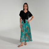 Woman wearing a black top and teal floral skirt on a gray background