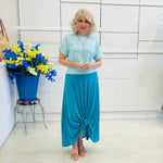 Woman in a blue outfit standing in a room with a white wall and decorative elements.