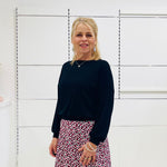 Woman in black top and printed skirt standing in a white room 