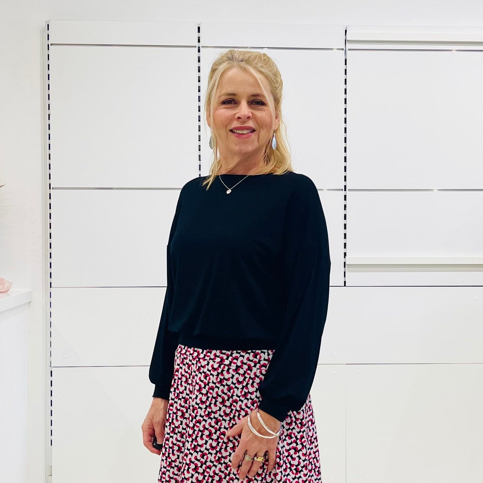 Woman in black top and printed skirt standing in a white room 