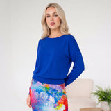 Woman wearing a blue top and colorful skirt in a minimalistic room.