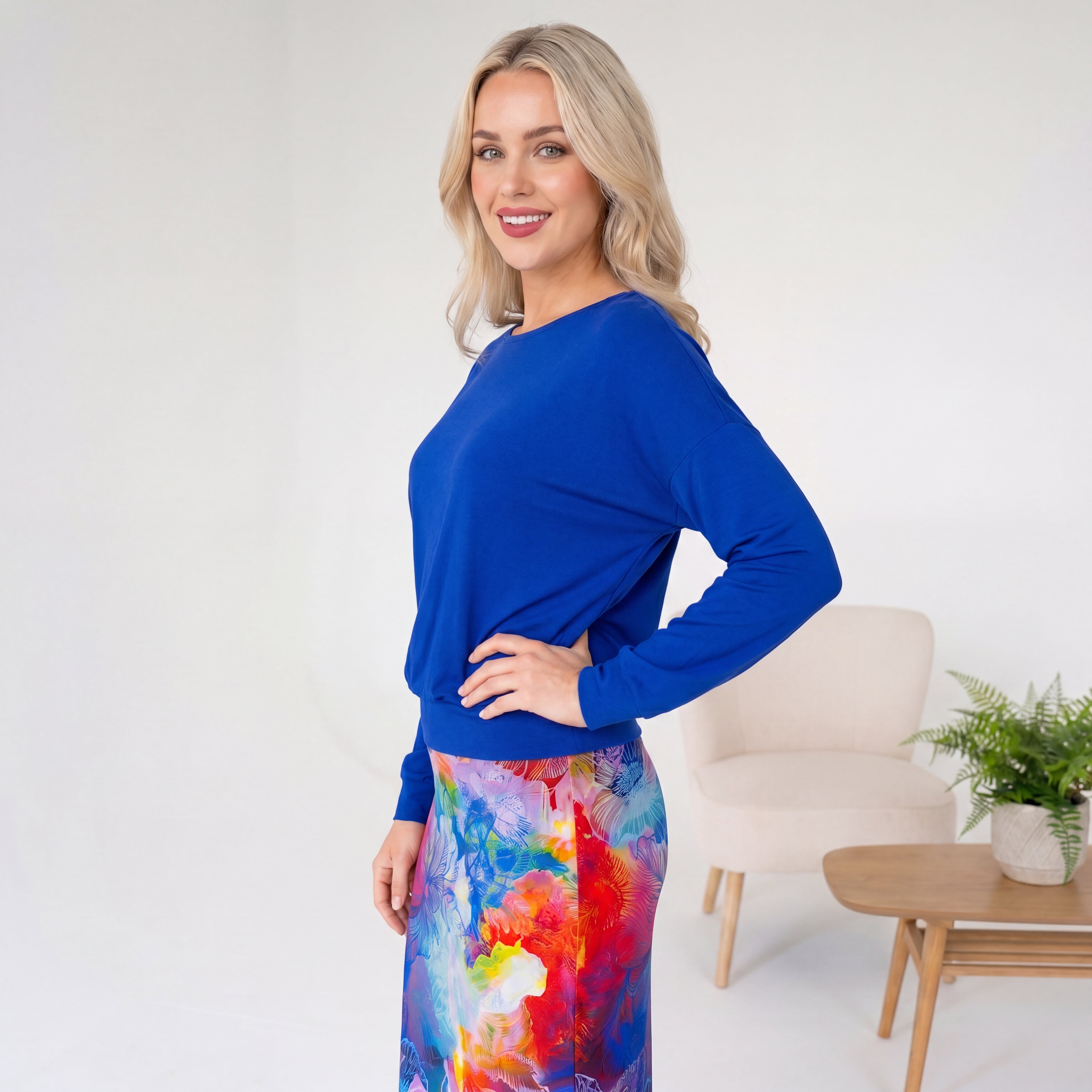 Woman wearing a blue top and colorful skirt in a minimalistic room.
