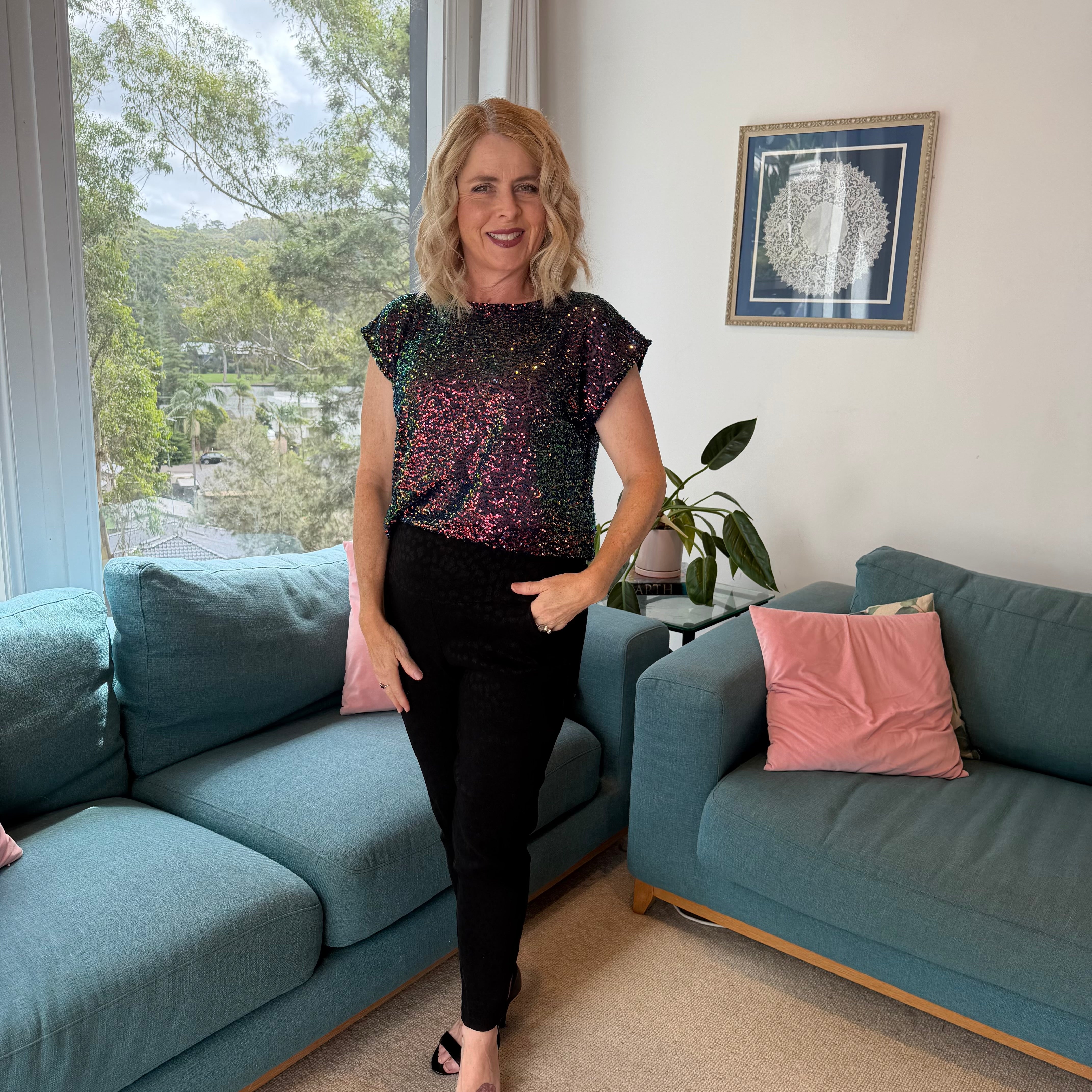 Woman standing in a living room with blue sofas and a window view.