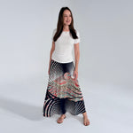 Woman wearing a long, patterned skirt with a white top on a plain background