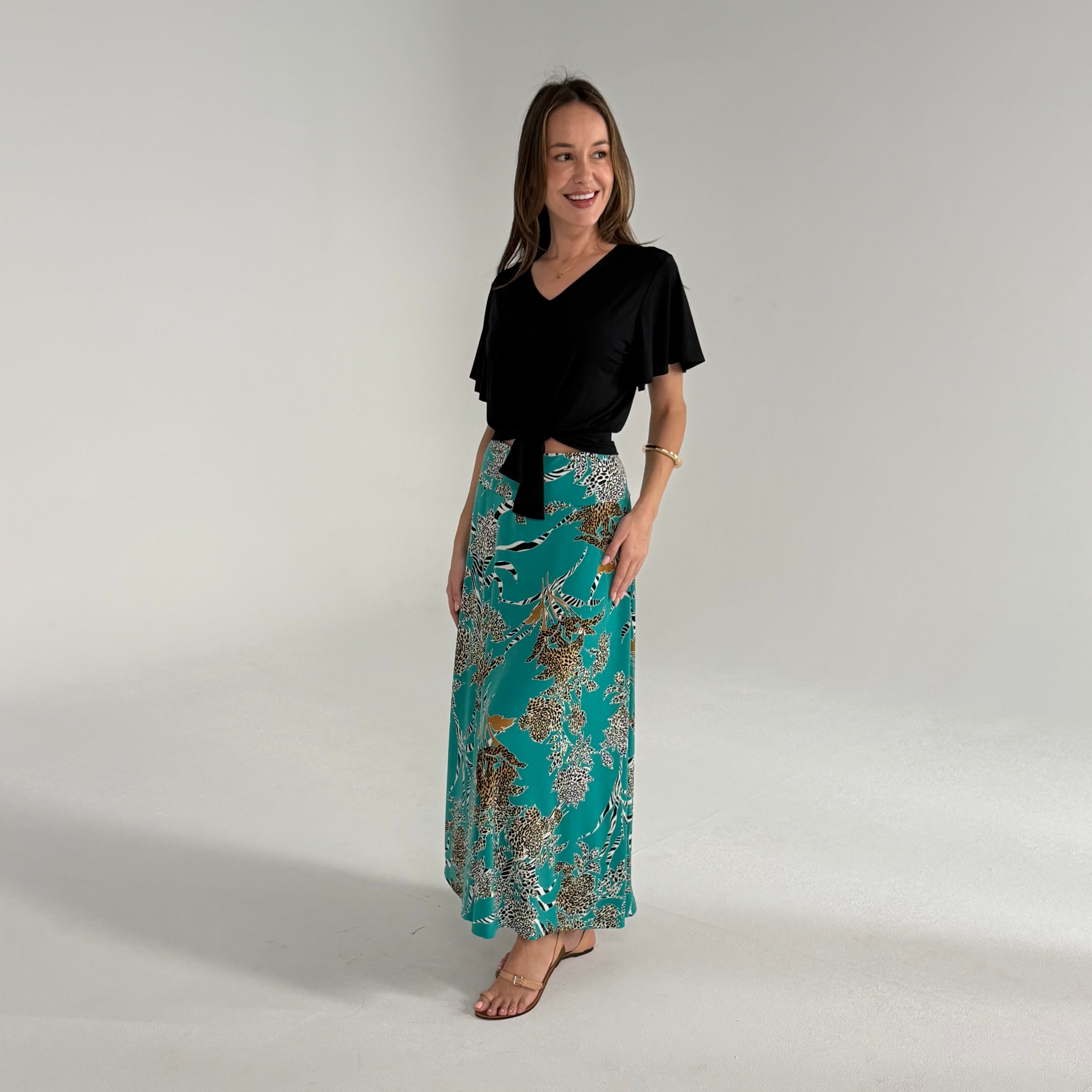 Woman wearing a black top and teal patterned skirt on a plain background