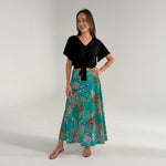 Woman wearing a black top and teal patterned skirt on a white background