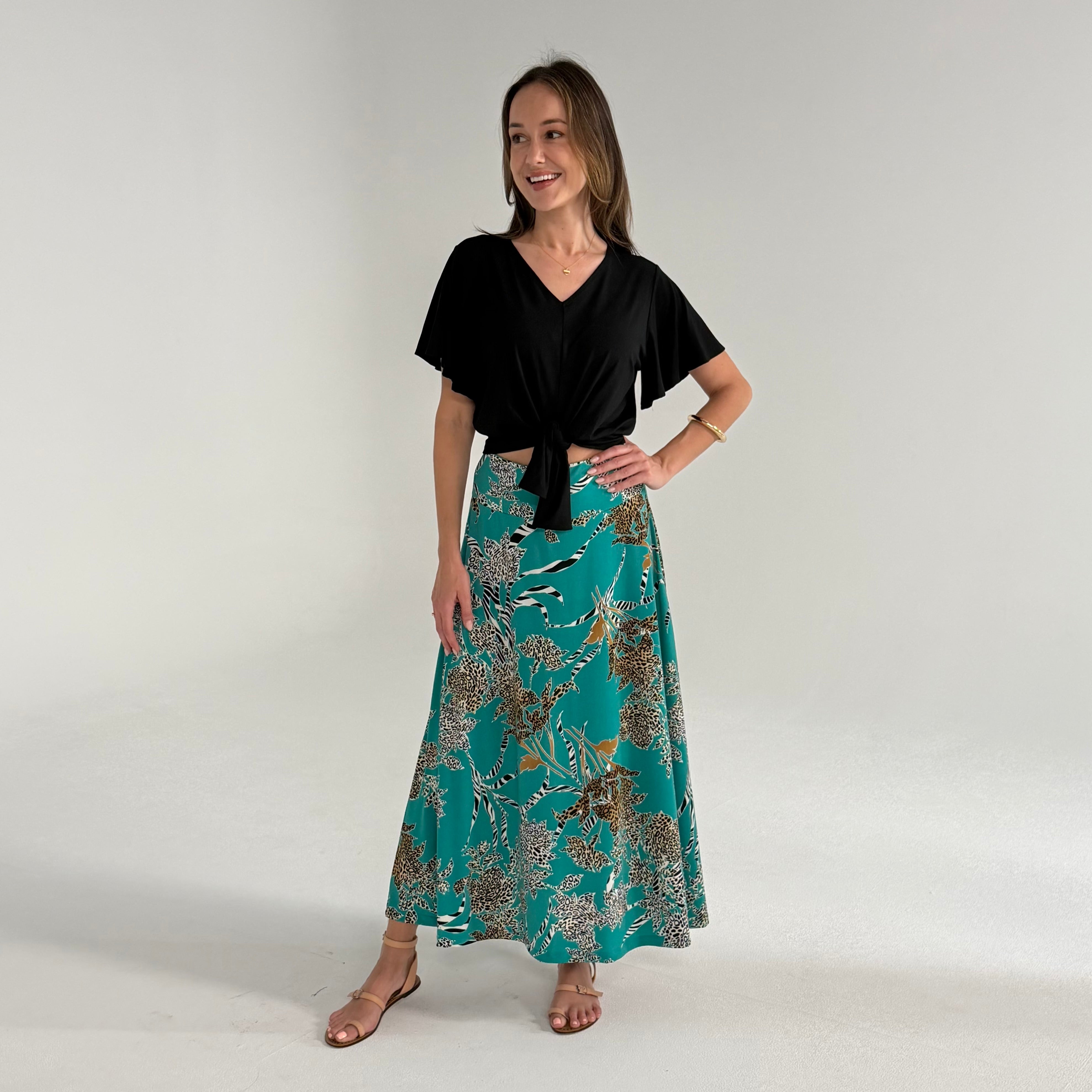 Woman wearing a black top and teal patterned skirt on a white background