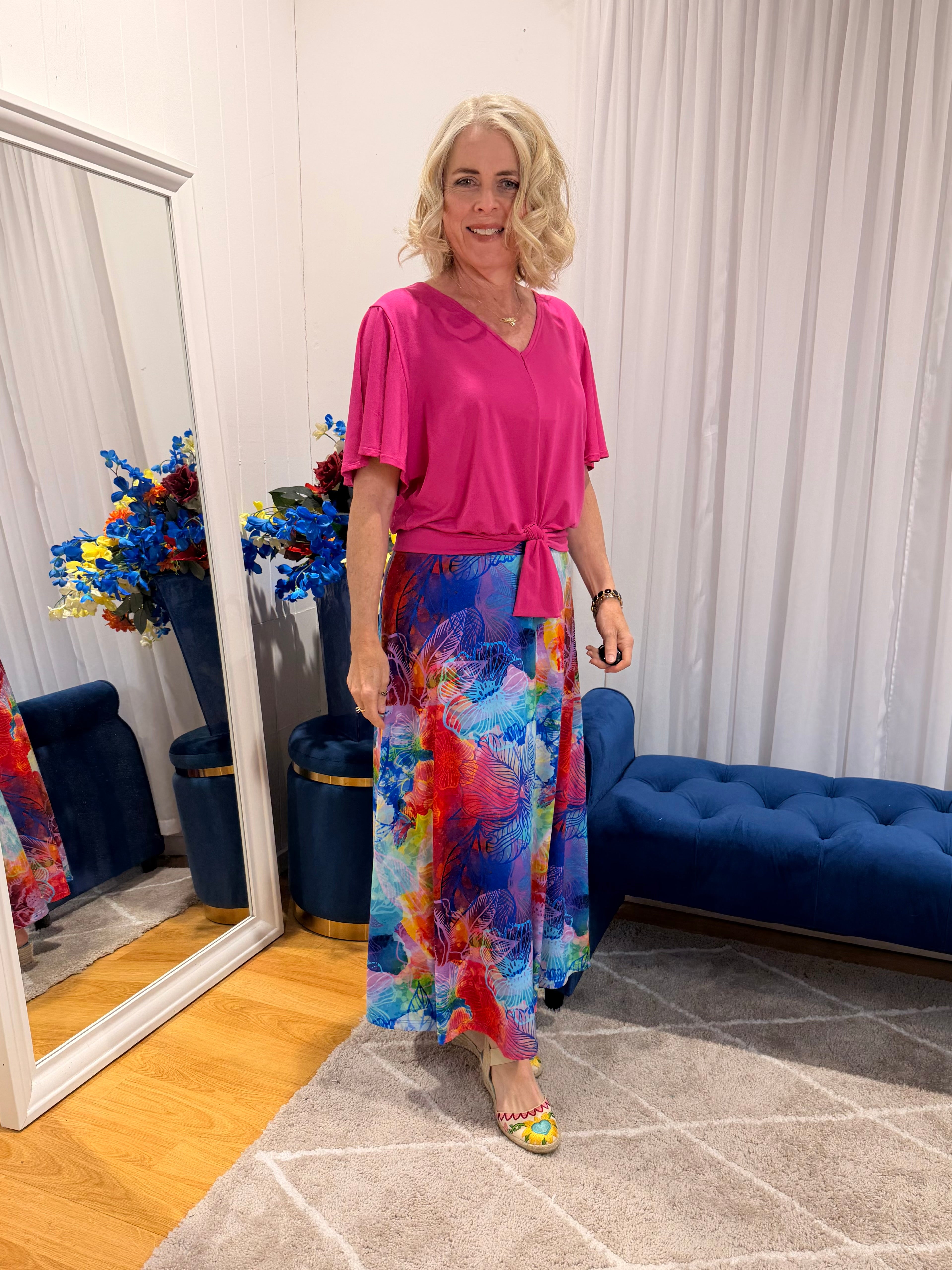 Woman wearing pink short sleeve top and colourful skirt.