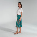 Woman wearing a white top and teal patterned skirt on a plain background