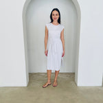 Woman in a white dress standing in a minimalistic setting with a white archway.
