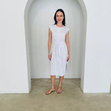 Woman in a white dress standing in a minimalistic setting with a white archway.