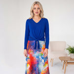 Woman wearing a blue top and colorful floral skirt in a minimalistic room.