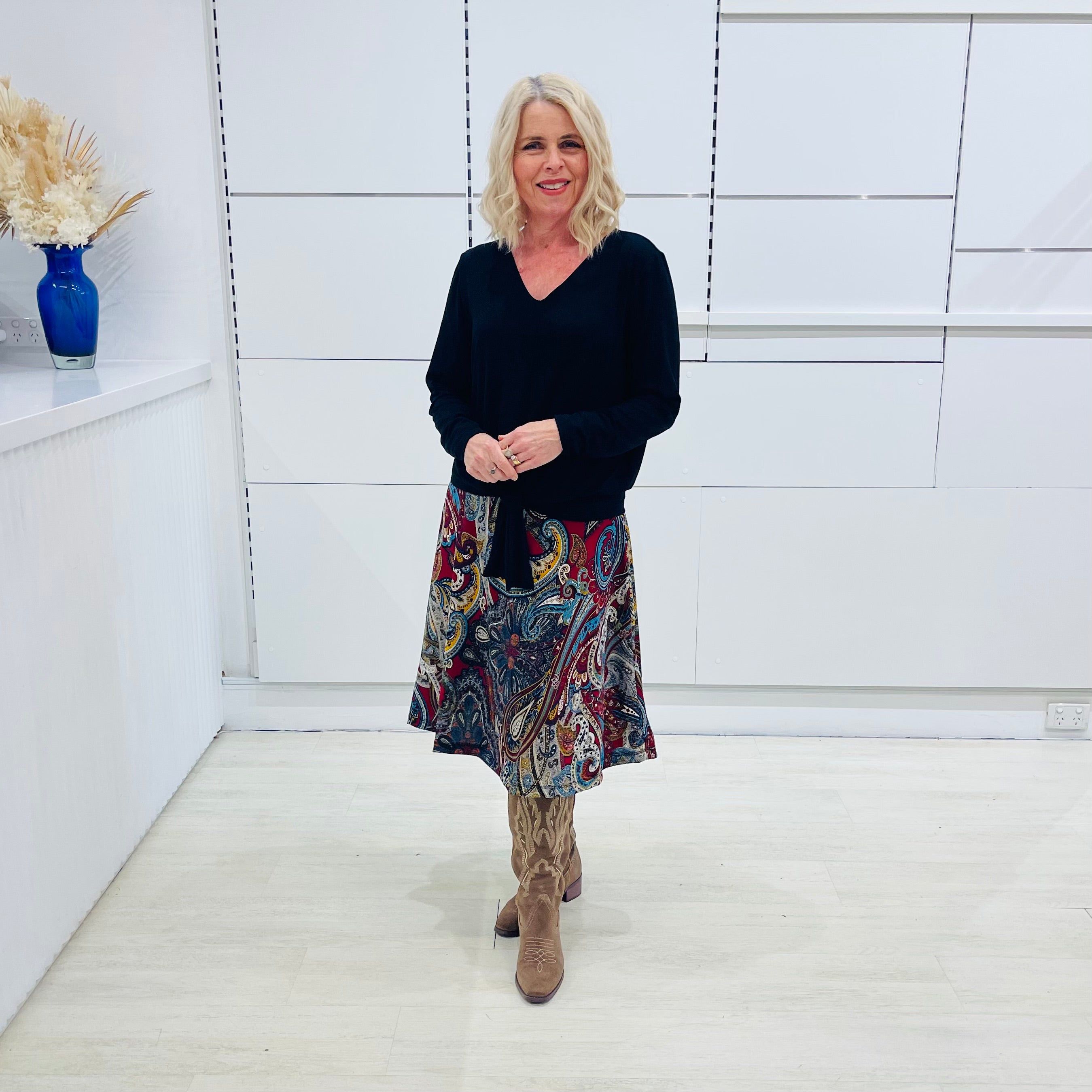 Woman wearing a black top and colorful skirt standing in a minimalistic room.