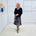 Woman wearing a black top and colorful skirt standing in a minimalistic room.