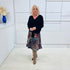 Woman wearing a black top and colorful skirt standing in a minimalistic room.
