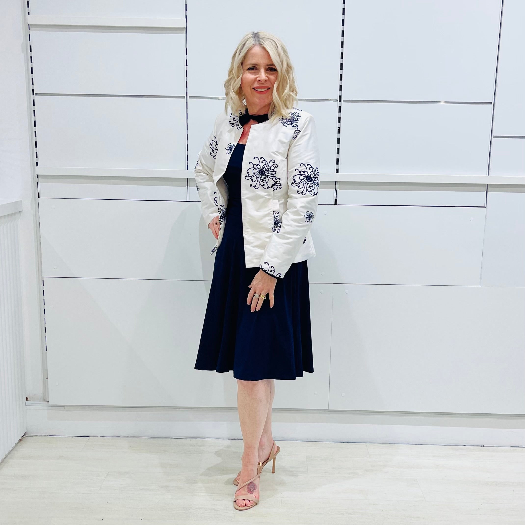 Penelope dress in deep navy blue, worn by model- elegant long sleeve design, knee length, with modern neckline, worn with Navy blue & white embroidered silk jacket, designed and Made in Australia.