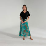 Woman wearing a black top and teal floral skirt on a plain background