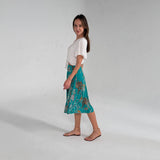 Woman wearing a white top and teal floral skirt on a plain background