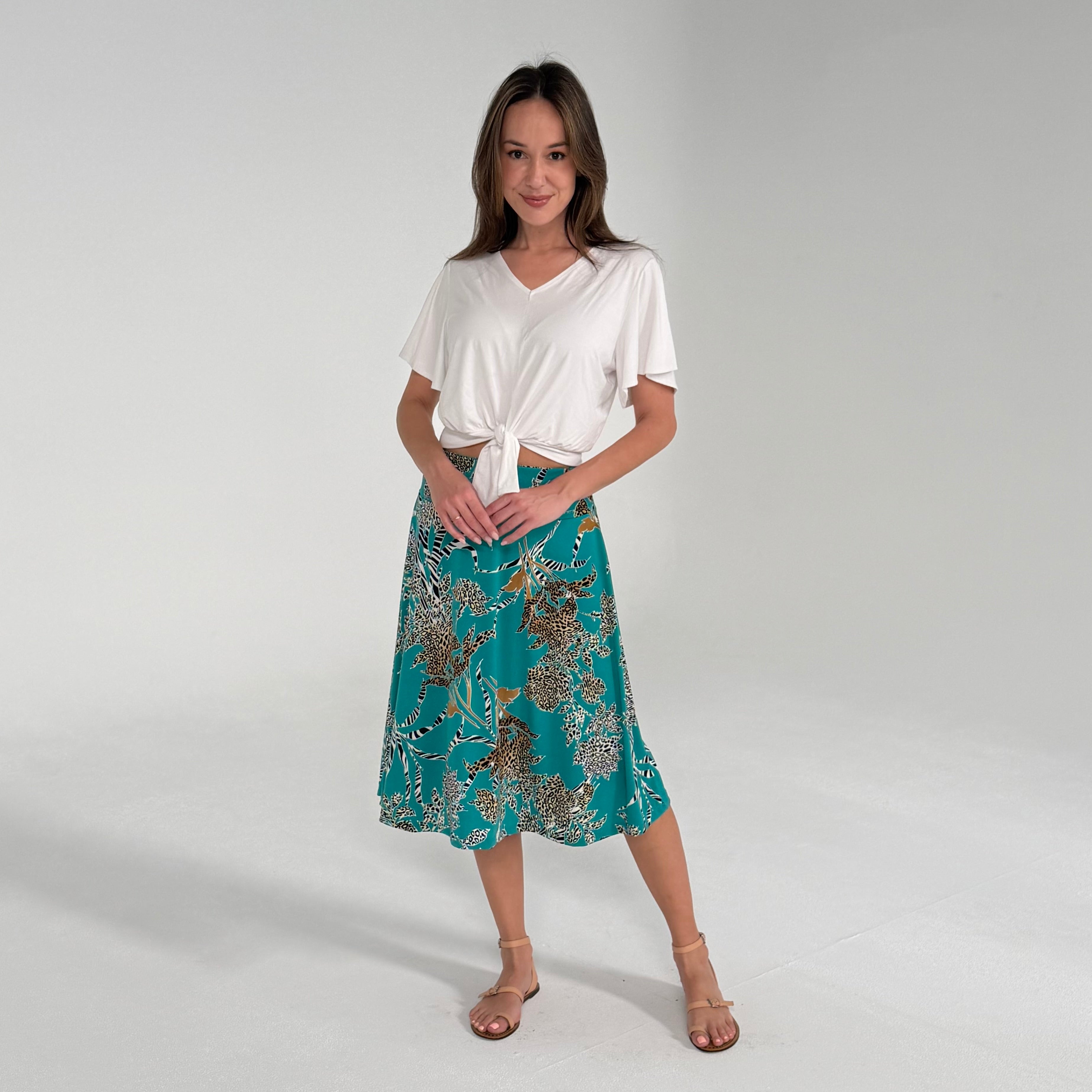 Woman wearing a white top and teal floral skirt on a plain background
