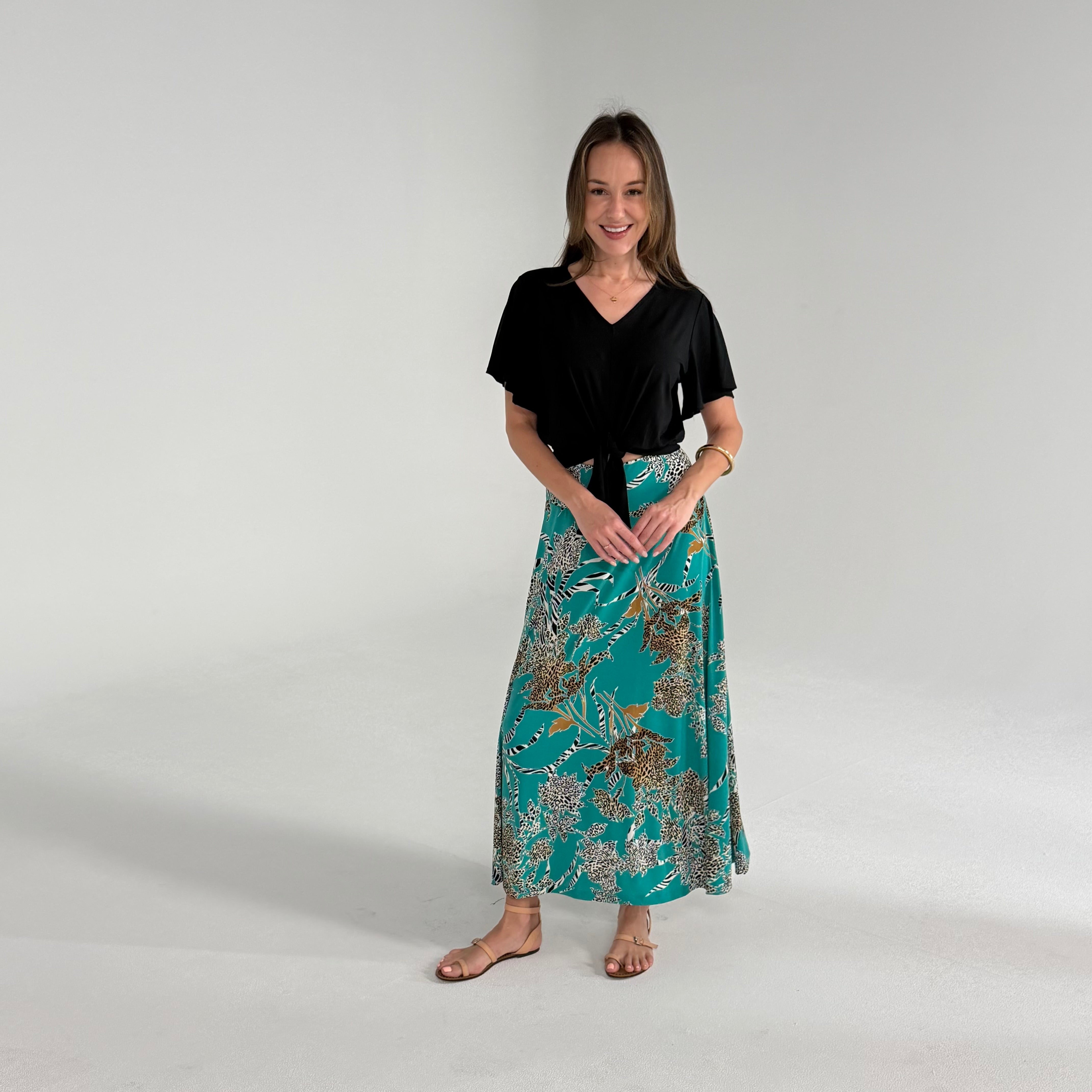 Woman wearing a black top and teal patterned skirt on a white background