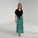 Woman wearing a black top and teal patterned skirt on a white background