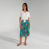 Woman wearing a white top and teal floral skirt on a plain background