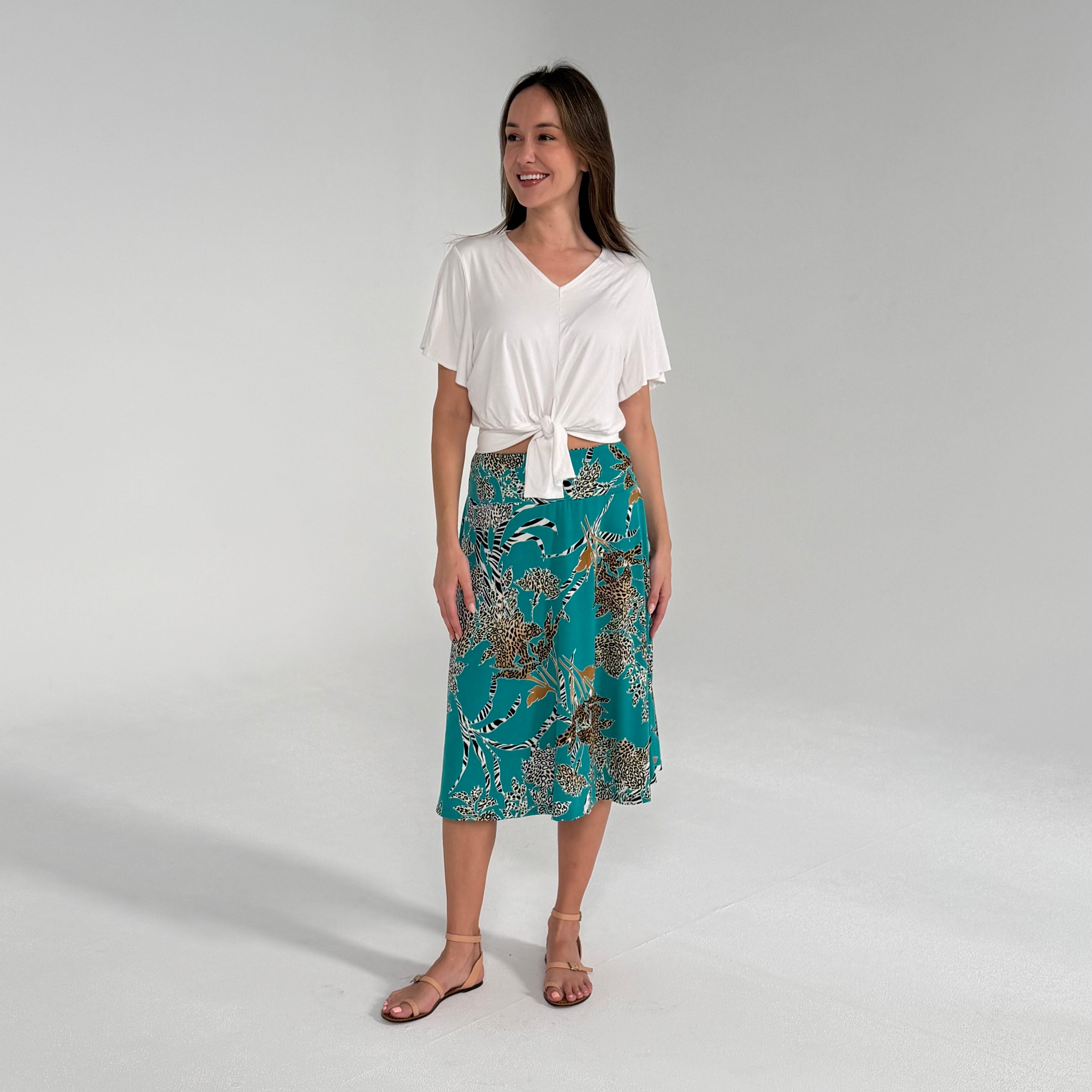 Woman wearing a white top and teal floral skirt on a plain background