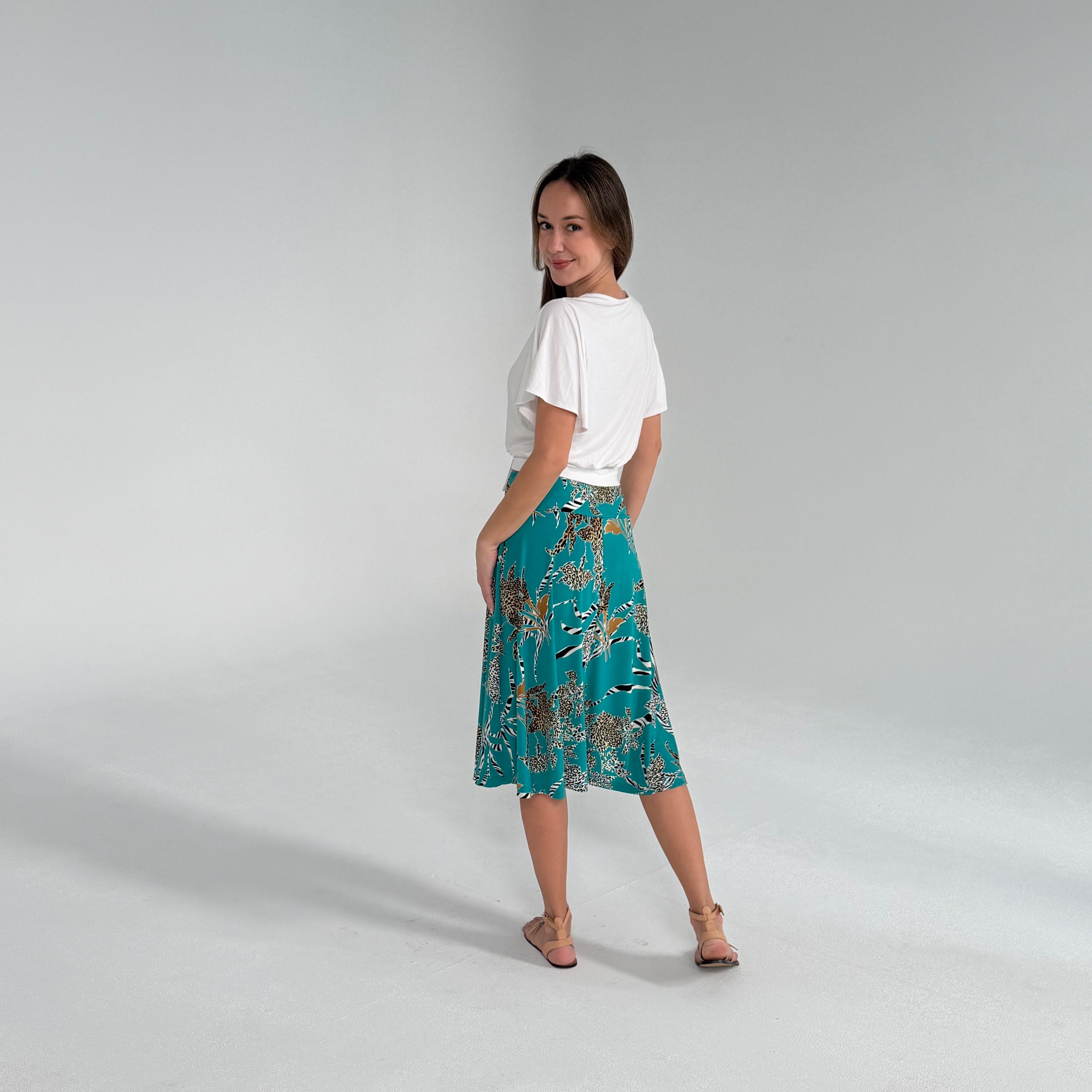 Woman wearing a white top and teal floral skirt on a gray background