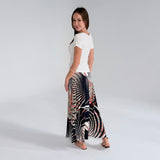 Woman wearing a white top and a long, patterned skirt on a plain background