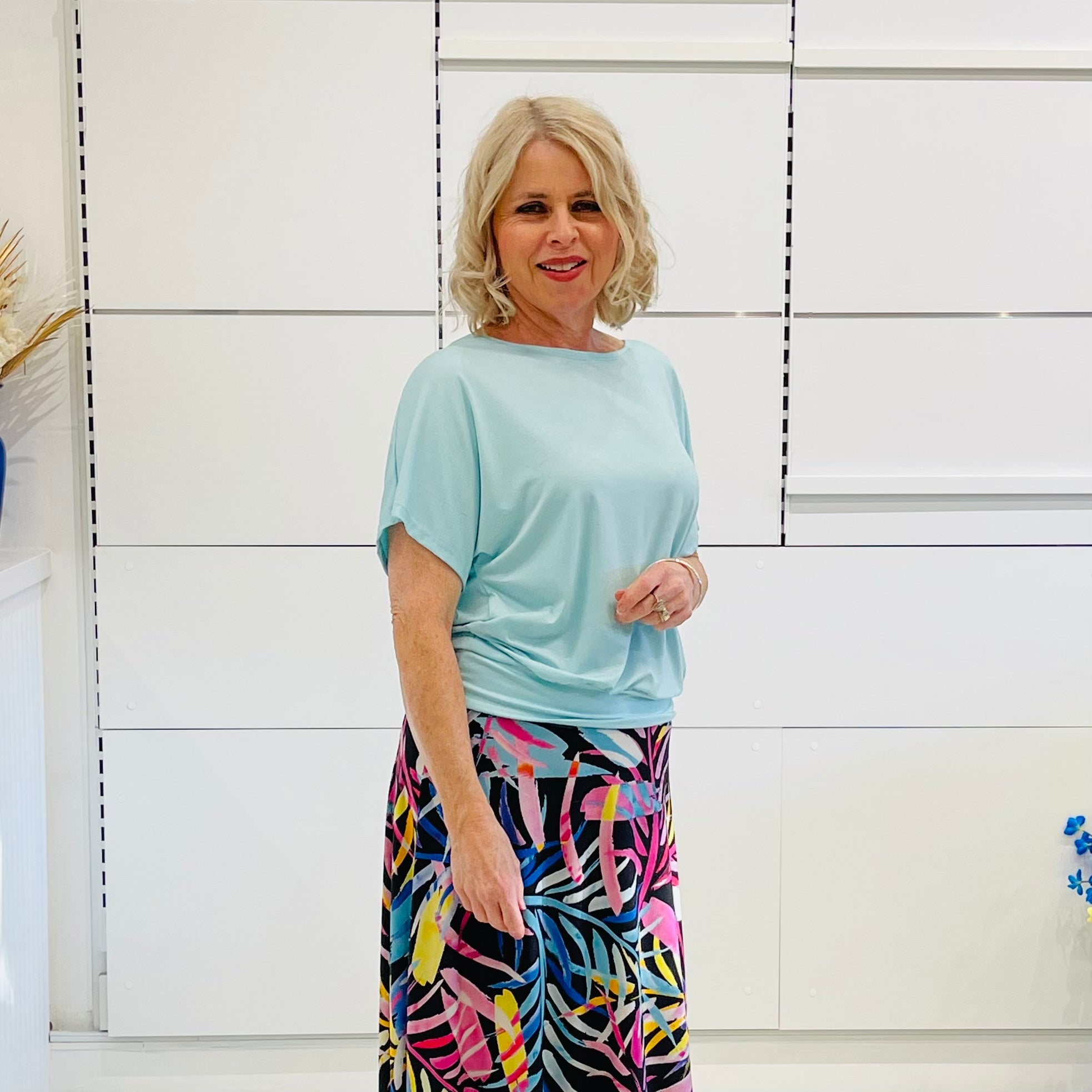 Woman wearing a light blue top and colorful skirt against a white background