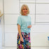 Woman wearing a light blue top and colorful skirt against a white background
