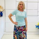 Woman wearing a light green top and colorful skirt indoors.