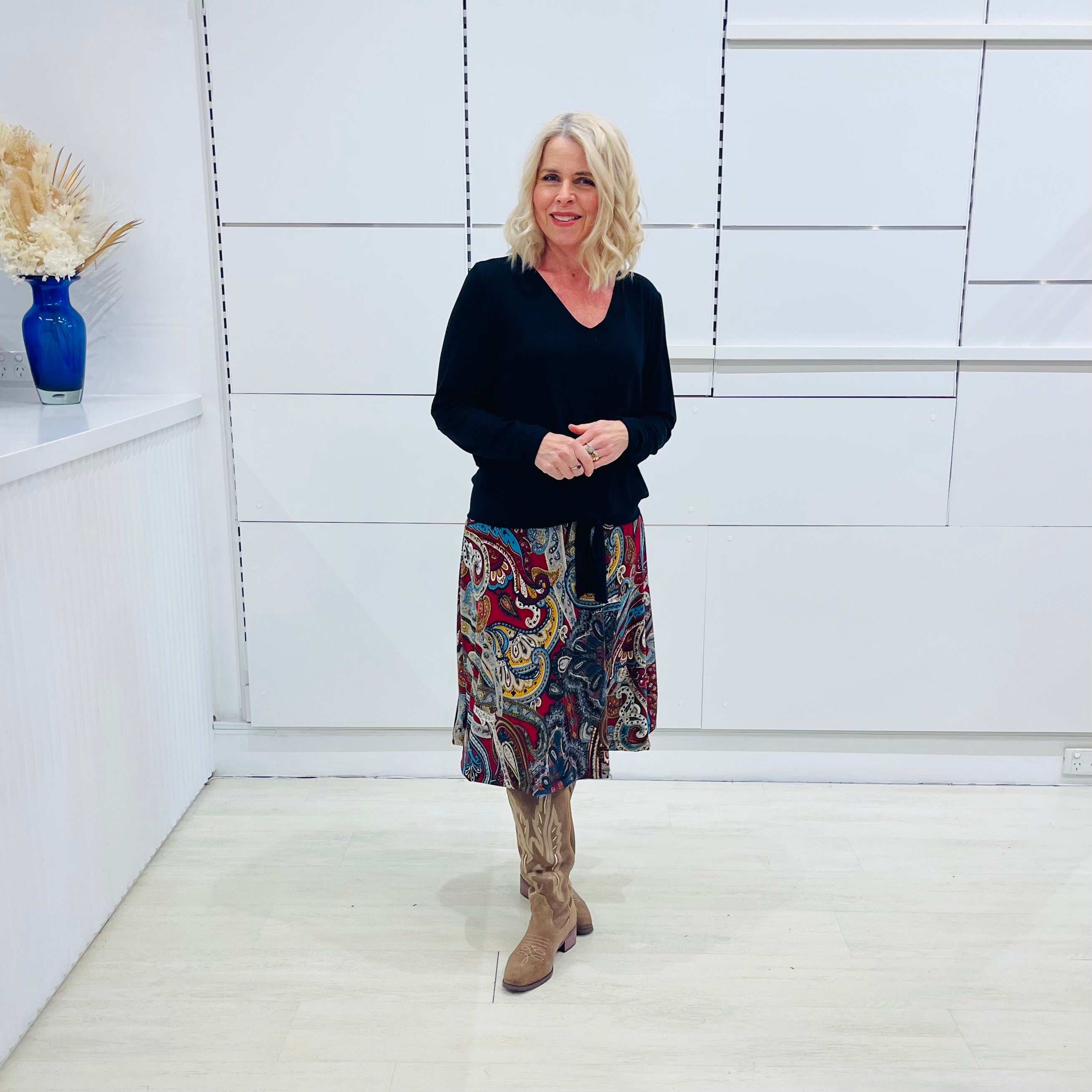 Woman standing in a minimalistic room with a white wall and light-colored floor.