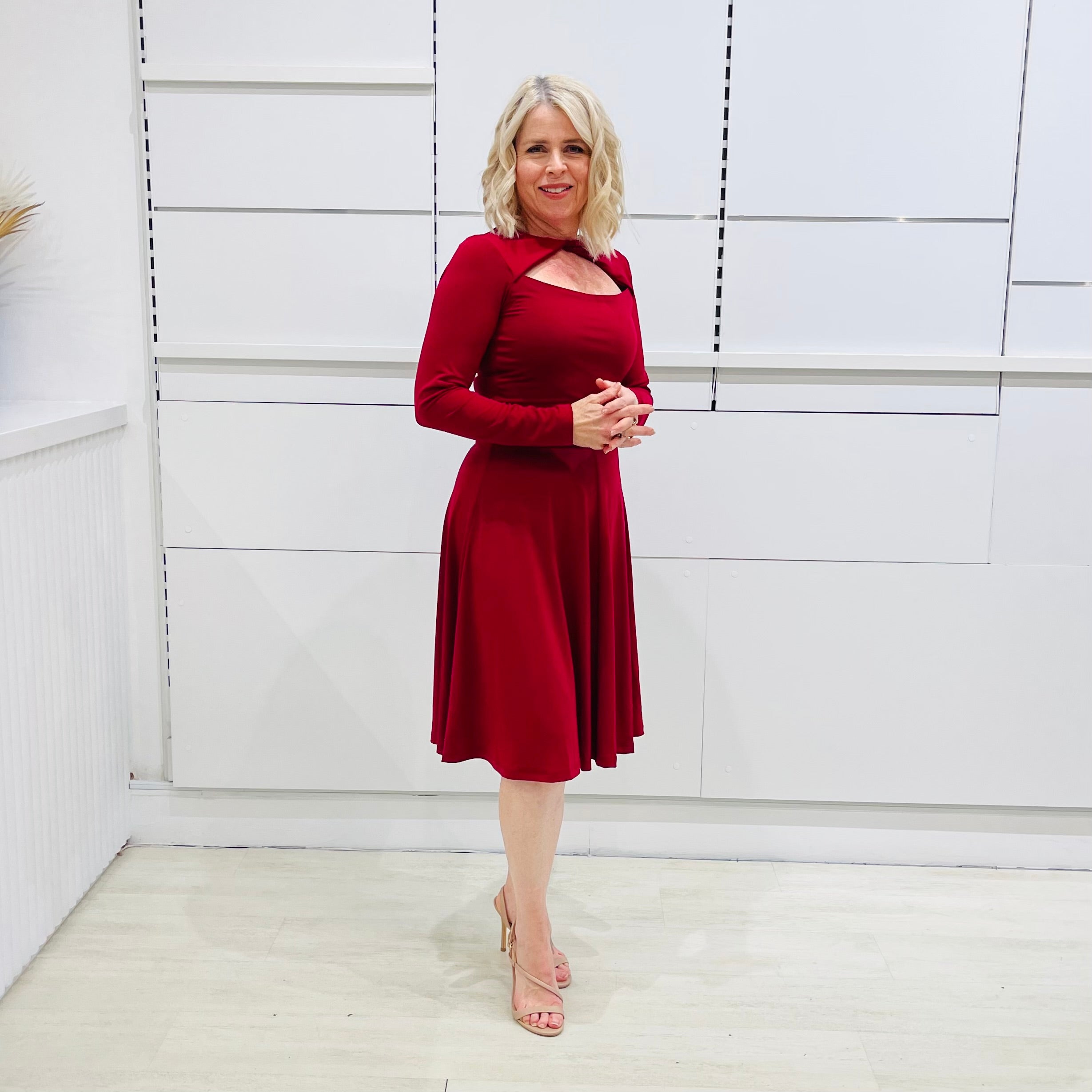 Woman wearing the Penelope dress n rich ruby red, featuring a fit-and-flare, knee length, slihouette, full length sleeves, and a cut out neckline.