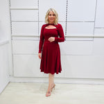 Woman wearing the Penelope dress n rich ruby red, featuring a fit-and-flare, knee length, slihouette, full length sleeves, and a cut out neckline.
