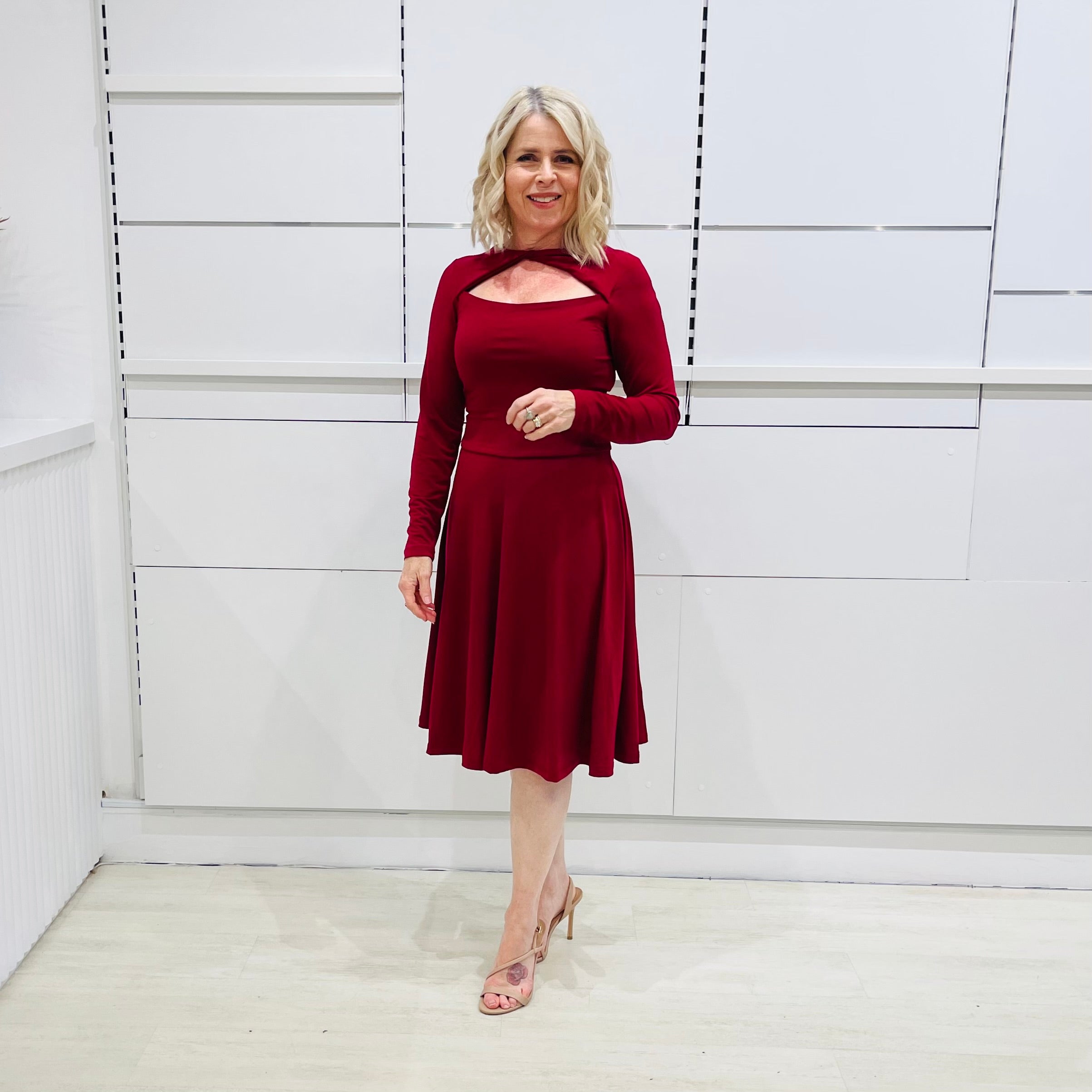 Woman wearing the Penelope dress n rich ruby red, featuring a fit-and-flare, knee length, slihouette, full length sleeves, and a cut out neckline.